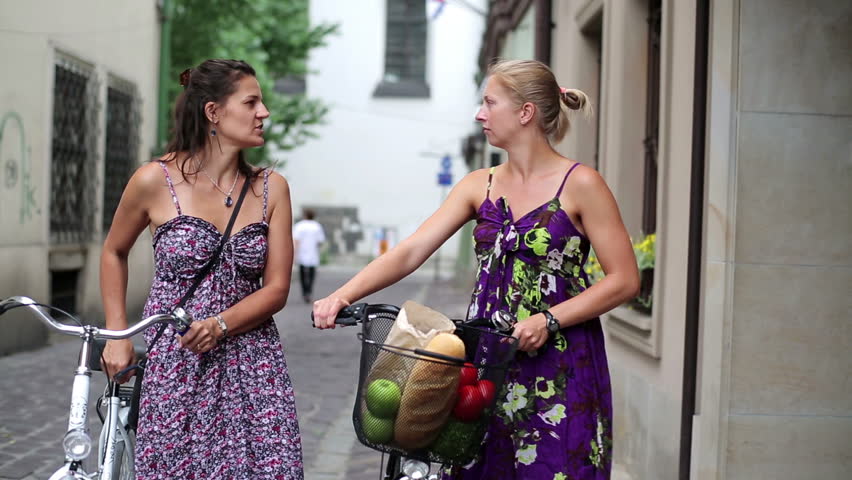 Happy female friends walking with bicycles in the city, steadycam

