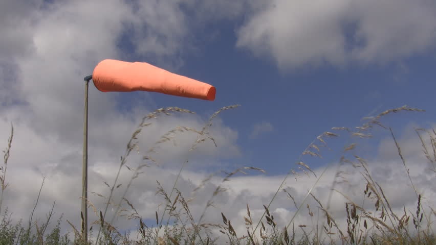 Orange wind direction indicator is flowing in the cloudy sky with a grass in front