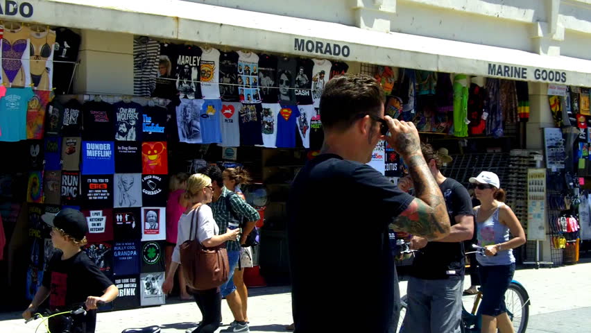 VENICE BEACH, CA - AUGUST 2: Tourists walk by Venice Beach Boardwalk merchant stores with T-shirts and souvenirs on August 2, 2012 in Venice Beach, CA.