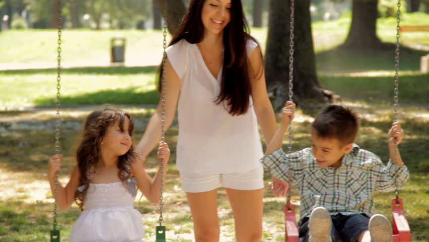 Beautiful mother swings her two little children on a swing.