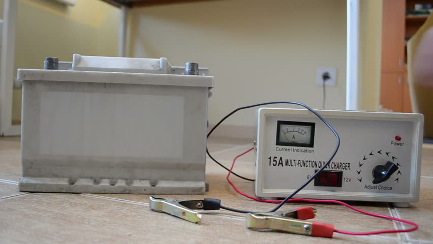Charging auto battery at home. Hand put charger clamps on accumulator plus and minus.
