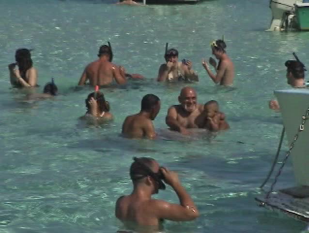 video of tour boats at Stingray Sandbar City in Grand Cayman Island. Man holding baby in water.