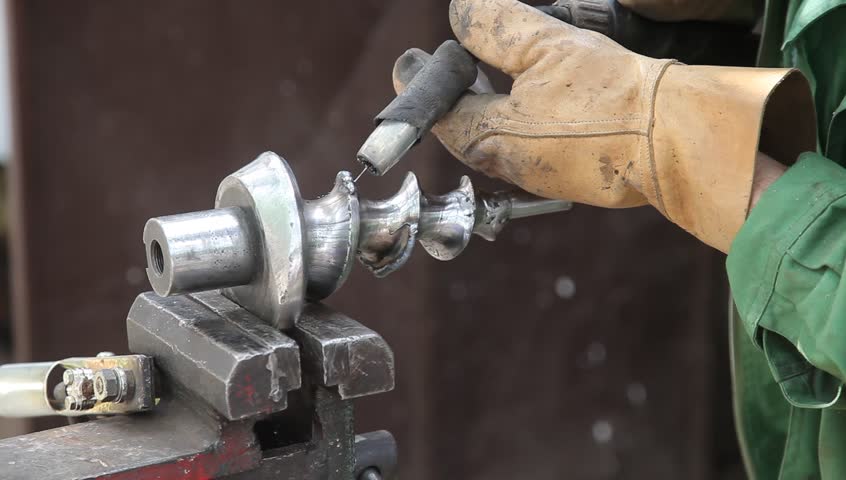 Arc welding of a steel shaft with helicoid, welder hands in gloves and tool