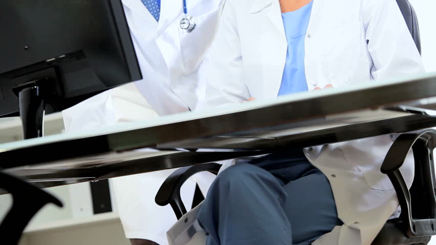 Caucasian hospital team discussing patient clinical trial results showing on computer monitor