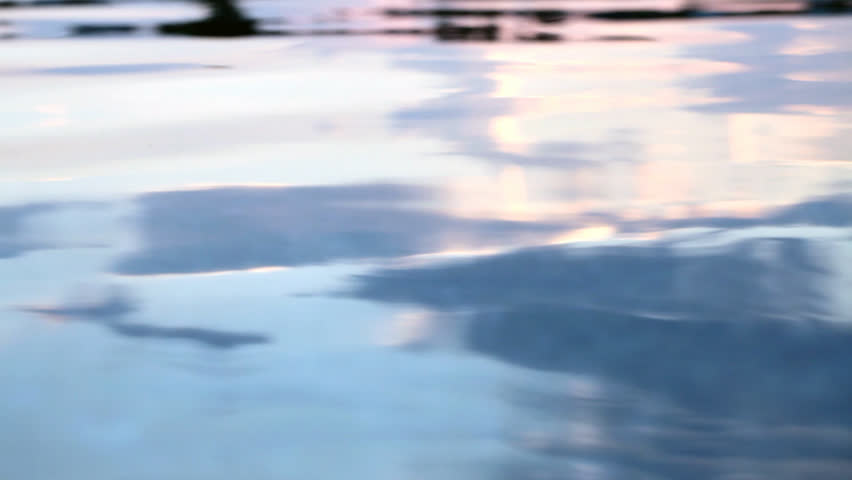 From dusk colored water surface in motion by gentle waves and some waterdrops (raindrops) falling.
