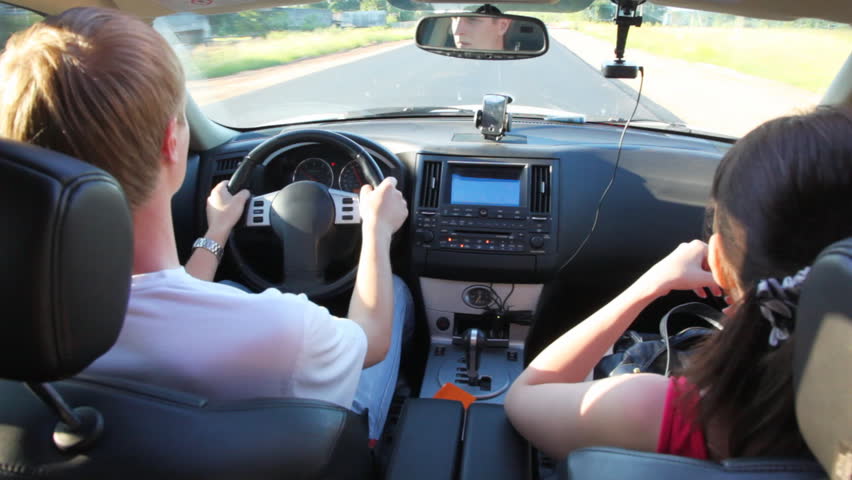 guy drives car going on road, and girl nearby sits