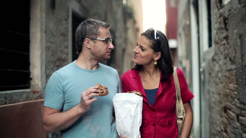 Happy couple walking and eating cookies in the city, stabilized shot