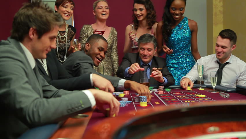 Men placing bets at roulette table watched by women in casino