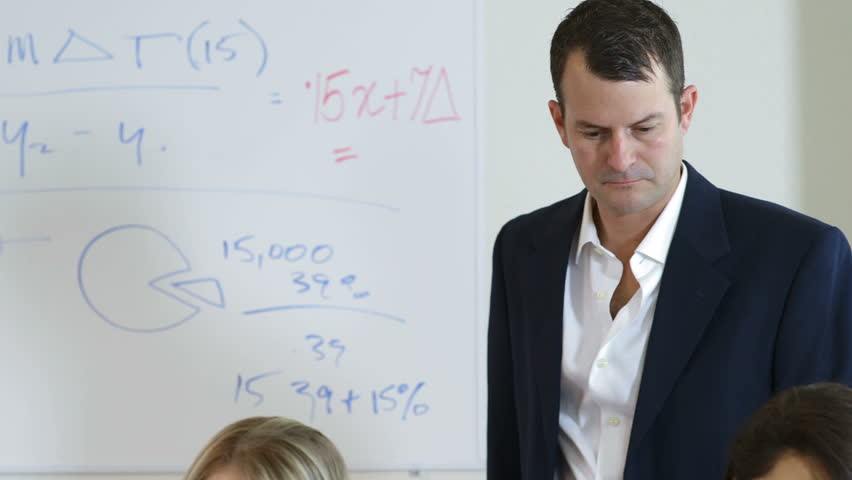 A college professor helps one of two pretty female students with her assignment. Camera tilts down and tracks action slightly left and right