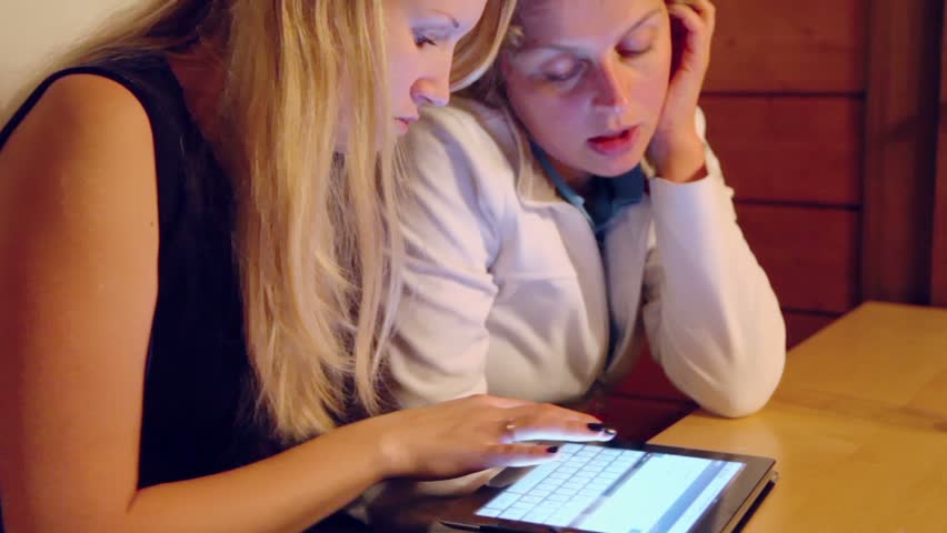 Pair of women use tablet pc at wooden table, closeup view