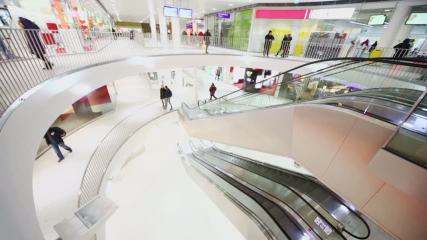 People walk near escalators on few levels of shopping center, view from above
