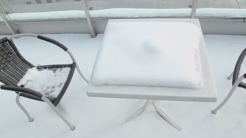 Chairs an table covered by snow at balcony near Europe square in Vienna, shown in motion