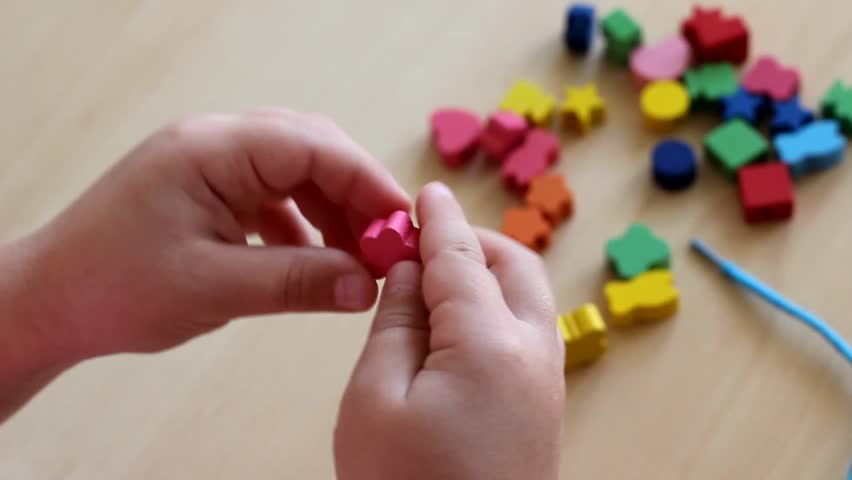 Little girl playing with beads and a string at the table