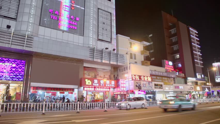 GUANGZHOU - NOV 21: Traffic on street and citizens walk by pavement with shops at night in city region Panyu on Nov 21, 2011, in Guangzhou, China. Guangzhou has population of over 14 million peoples