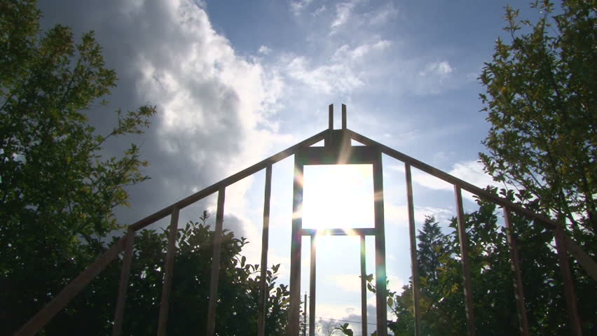 Camera tilt down revealing clouds and sun shining through window on framework of new construction.