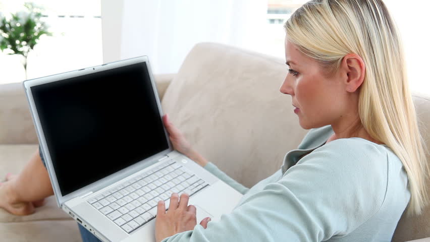 Blonde woman using a laptop while sitting on her couch