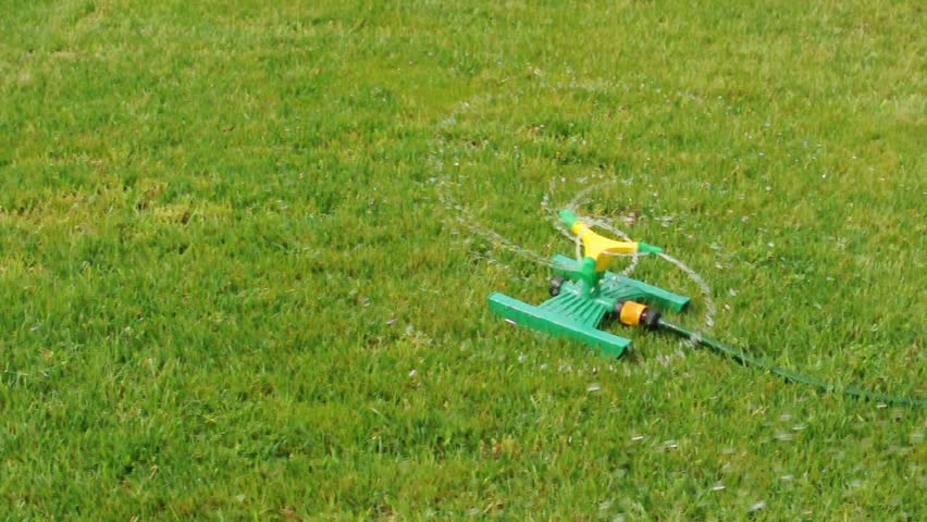 Lawn sprinkler splashing water over green grass.