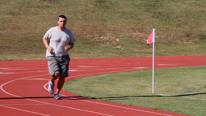 Overweight adult man runs a sports track for exercise and fitness to burn calories and lose weight.