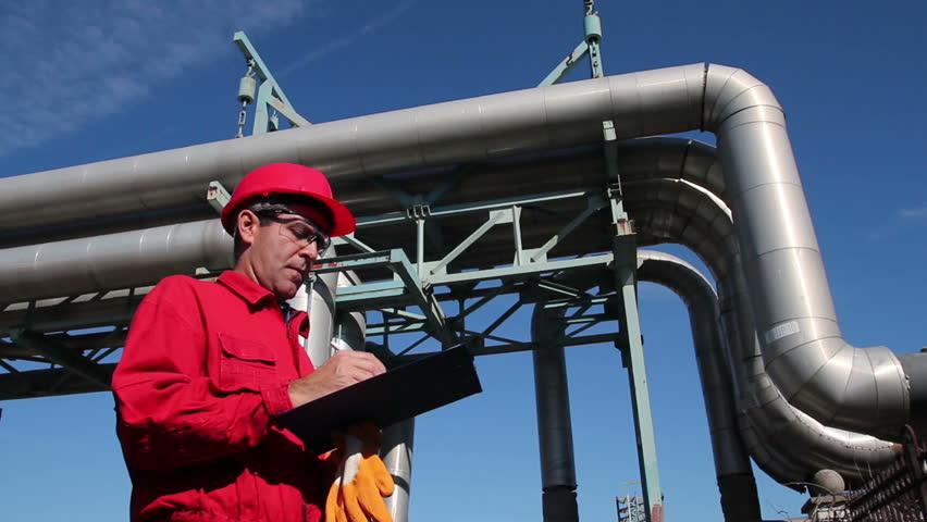 Refinery Worker and Pipelines.
Worker wearing red overalls and hardhat , writing on clipboard next to pipelines. HD1080p. 