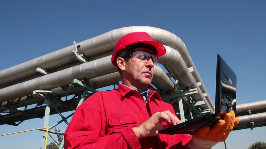 Petrochemical Engineer Using Laptop.
Engineer in red overalls and hardhat working in oil and gas refinery. HD1080p.