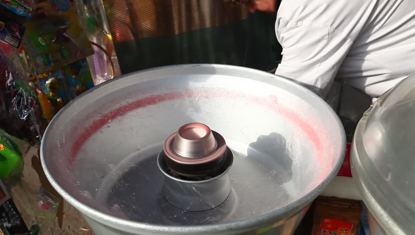 Cotton candy making in Bucharest, Romania. Strawberry flavor and red color. Daylight, outdoor, medium shot.
