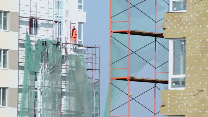 Labourer in orange uniform stands on falsework of dwelling house at construction site