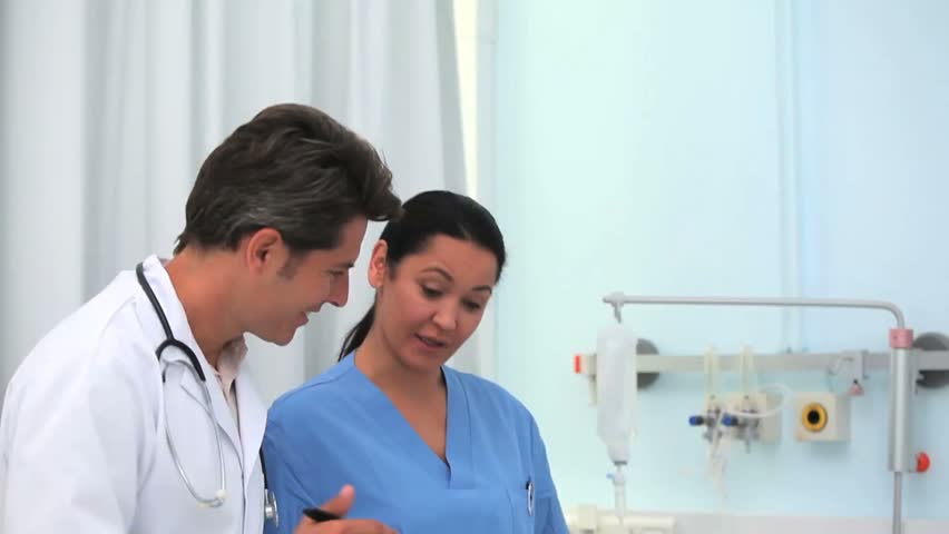 Doctor smiling while holding a clipboard in hospital ward