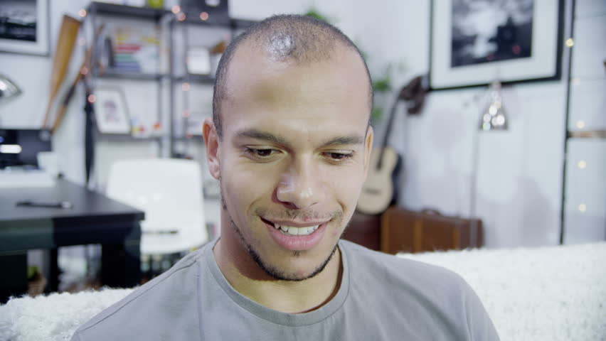 Computer screen's point of view of young man video chatting. Looking directly at camera for a close up shot and smiling and waving.