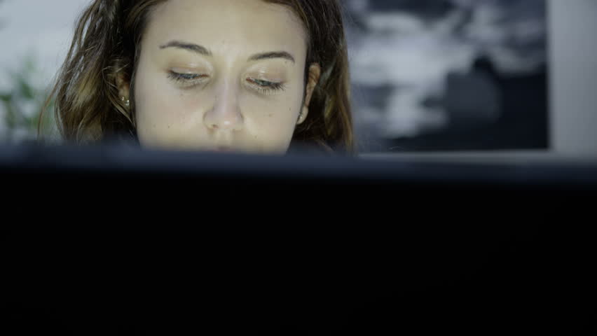 Close up of a very tired young woman who is working on a computer late into the night. She is over-worked and it is easy to see the emotional strain on her face. In slow motion.