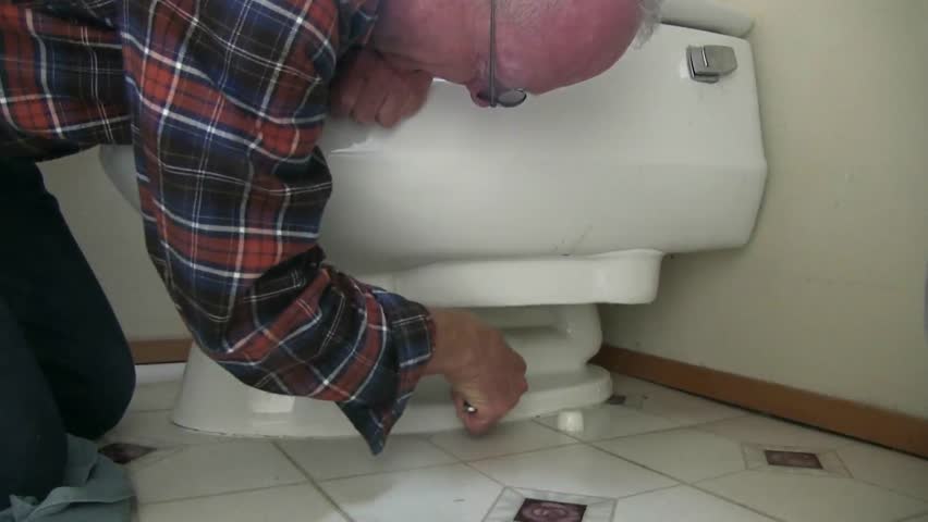 Senior plumber repairs toilet