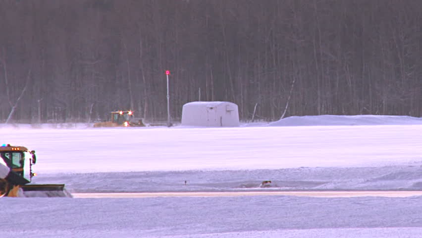 Long tight shot of a snow blower clearing snow from runway at Anchorage airport.
