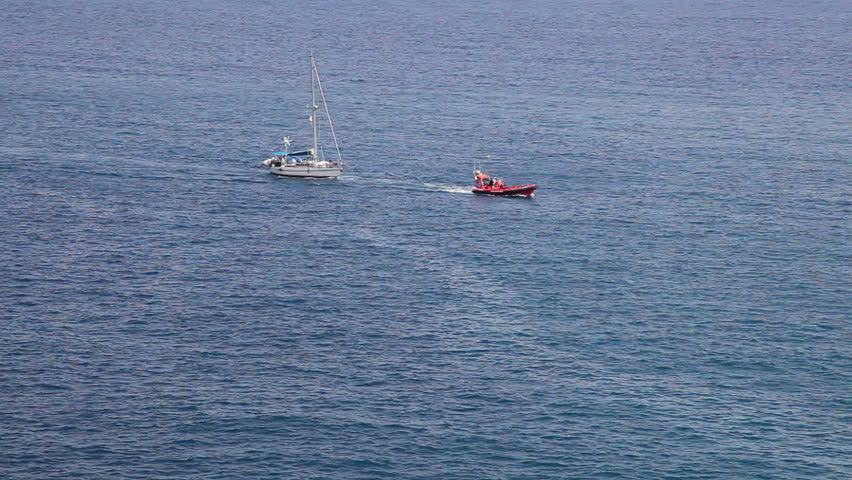 boat towing white yacht to port