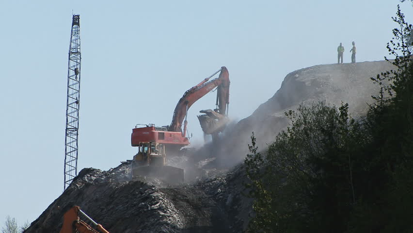 HOMER, AK - CIRCA 2012: A massive road construction project involving two large excavators, a bull dozer, a crane, and lots of workers and dust.