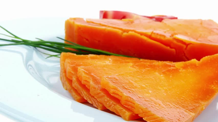orange aged delicious cheddar cheese chop with slice on blue plate with tomatoes and chives isolated over white background