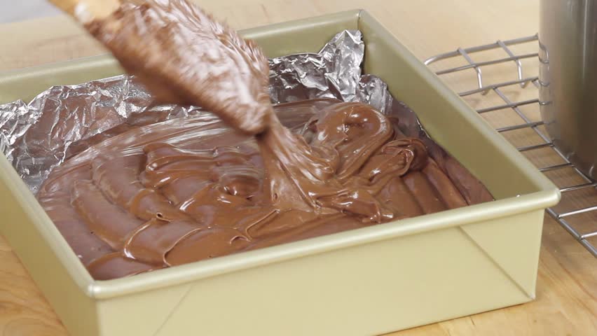 Chocolate fudge mixture being poured into a baking tin lined with aluminum foil