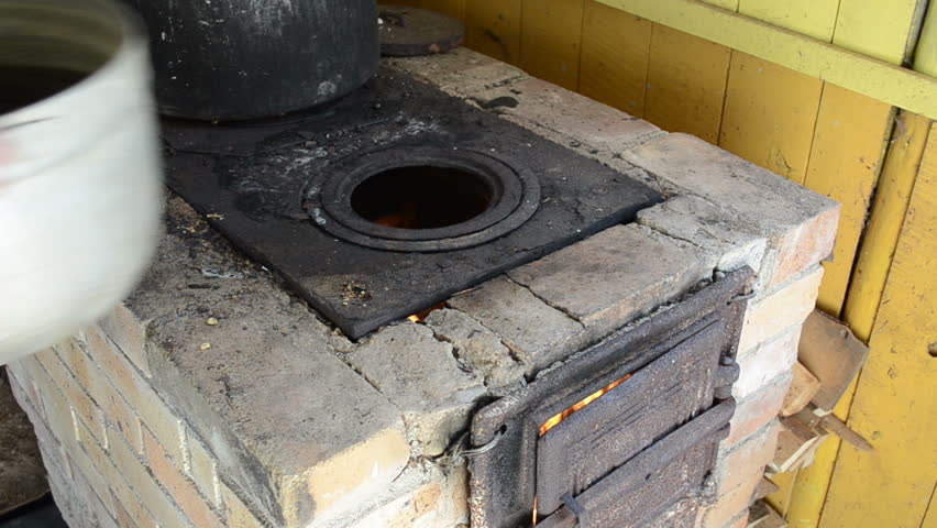 old rural kitchen furnace and firewood burning inside and hands put huge pot on it.