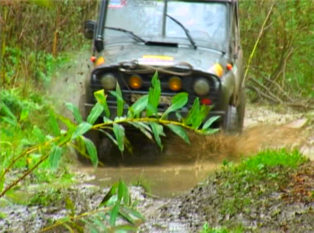 Off - road vehicle traveling across the big puddle. Green forest as a background. Slow-motion