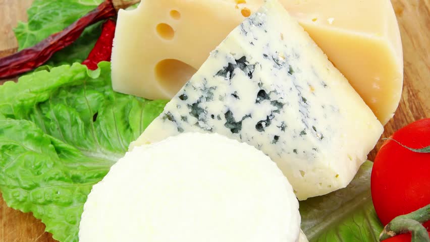 delicatessen cheeses on wooden board with vegetables olive oil and bread isolated over white background