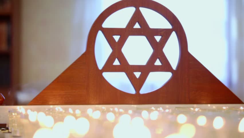 Many candles burn near wooden merkaba symbol at memorial