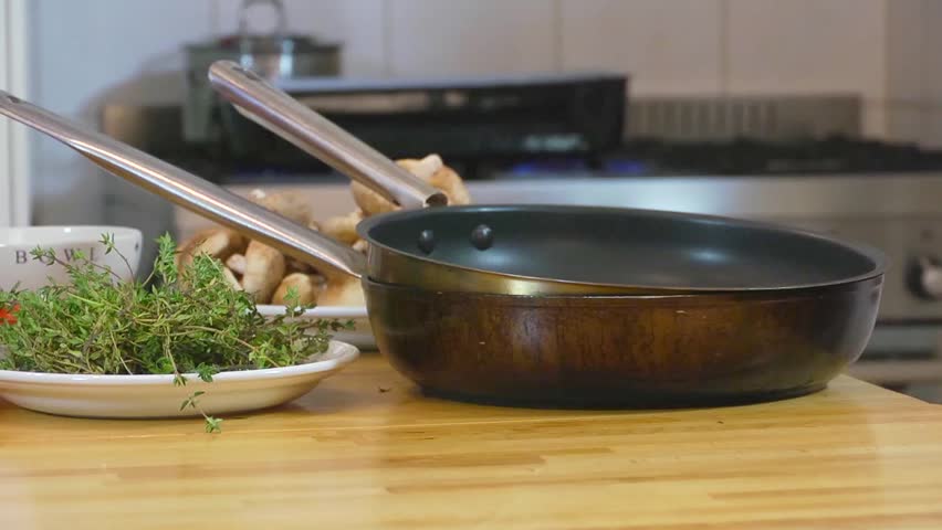 Pan over kitchen utensils, plates and bowls with freshly cut ingredients, ending at a chef, seasoning a large roast (haunch of venison)