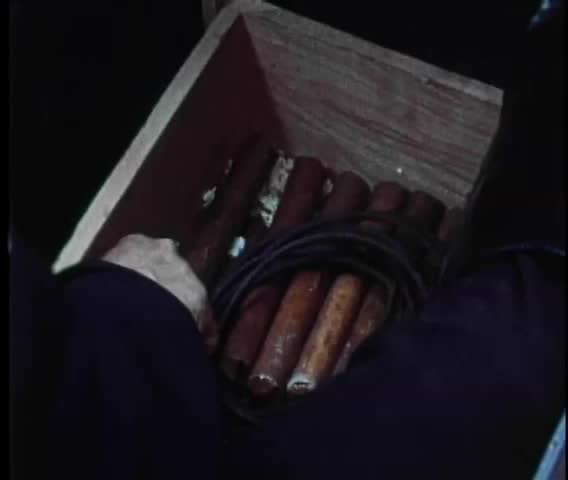 Close-up of man's hand picking up stick of dynamite from wooden box