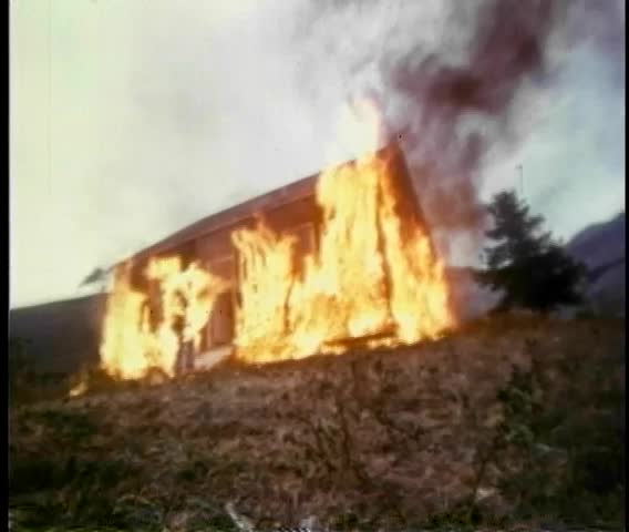 Stunt man on fire walking out of burning house on film set