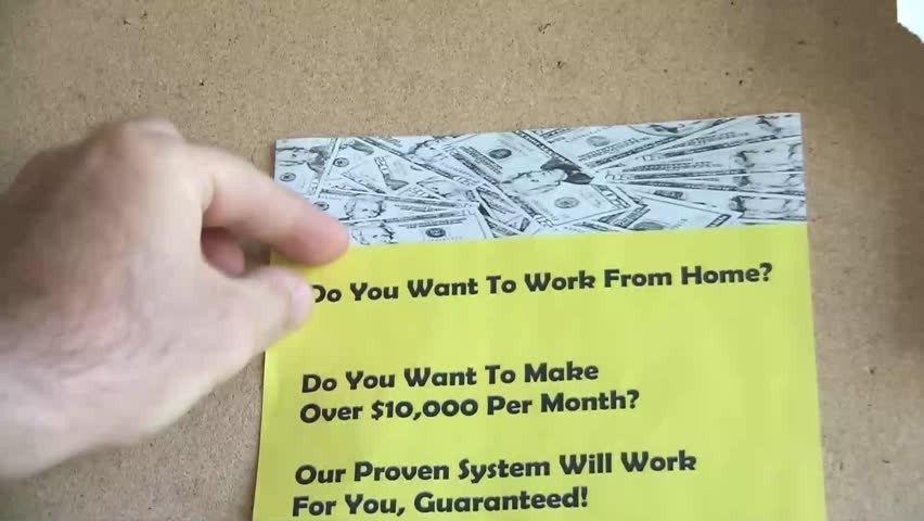 Hand pins up a yellow work from home flyer that asks whether reader wants to make over $10,000 per month.