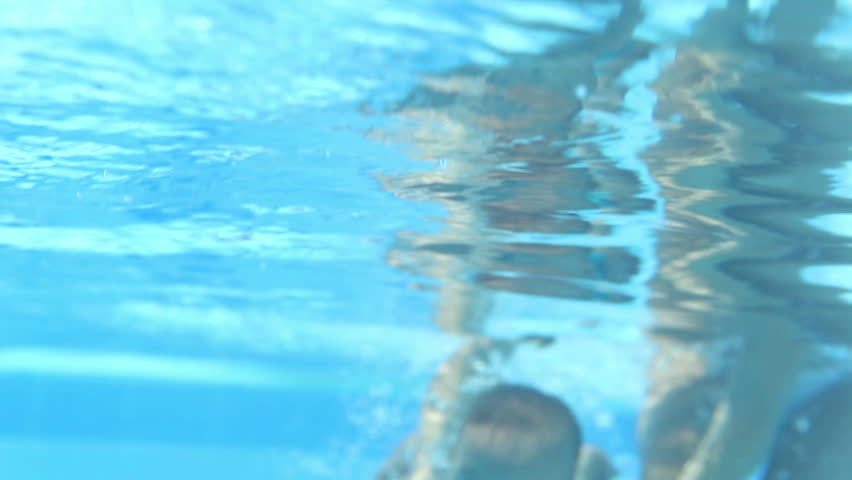 Beautiful happy mother teaching daughter to swim under water in swimming pool