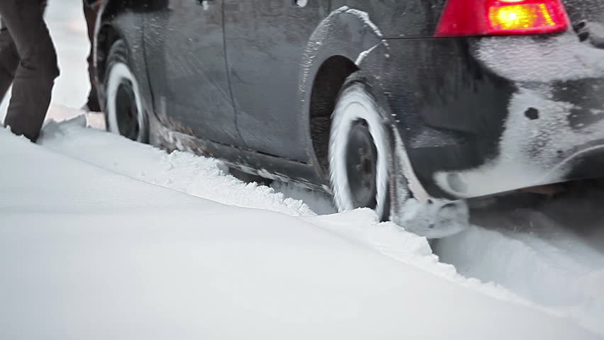 The car stalled on a snowy road and people kicking him out of a snowdrift