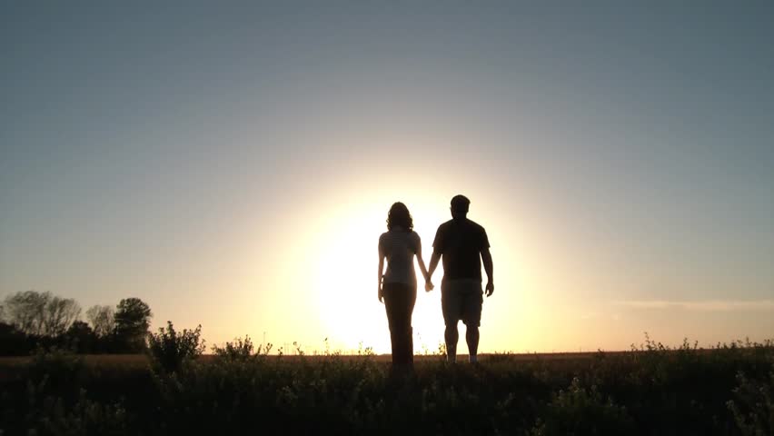 Couple walks into sun up hill and then stops to take in romantic scenery, put arms around each other, and then talk.