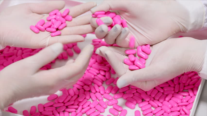 Lab technicians inspecting the quality of pills at a pharmaceutical plant.