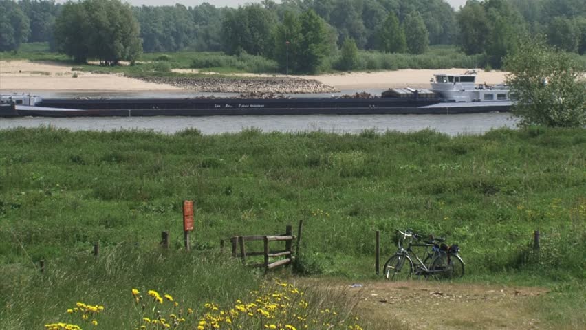 Cargo riverboat on Dutch River Waal,  low water level. Parked bike in pasture.