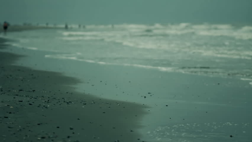 Alt. version with color correction. Waves wash up on shore on Isle of Palms (near Charleston, SC) in early morning low light. People walking on beach out of focus in distant background. Nat sound.
