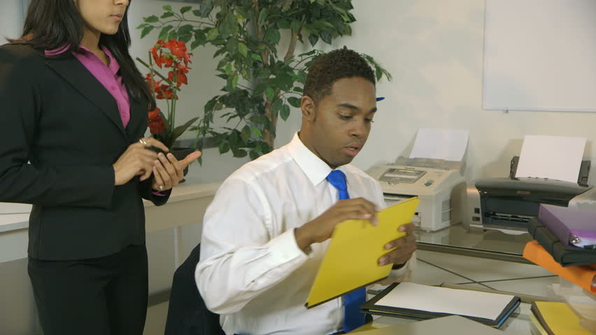 An annoyed business manager enters the office of her assistant who starts searching for a report she is waiting for. 